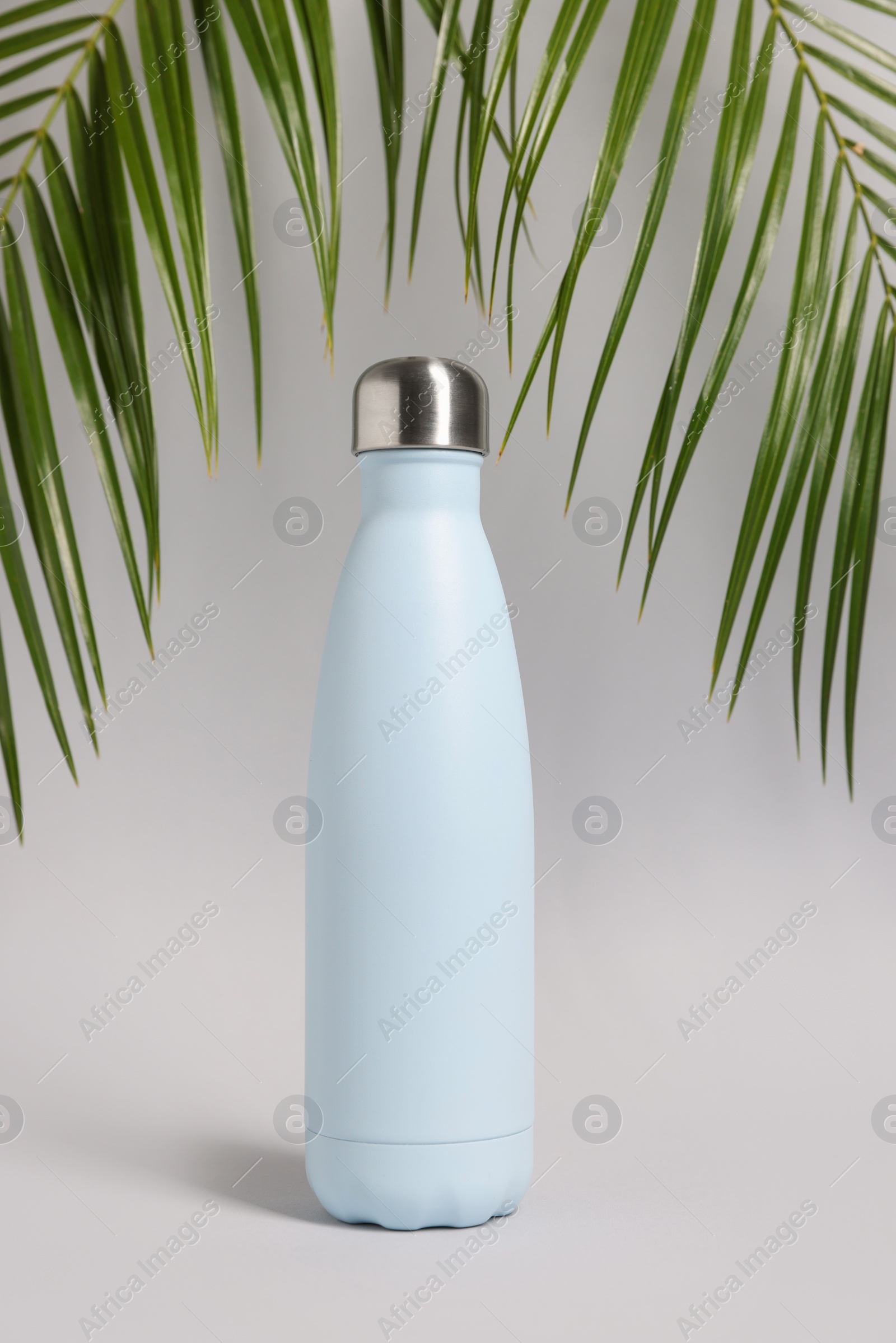 Photo of Stylish thermo bottle near tropical leaves on light grey background