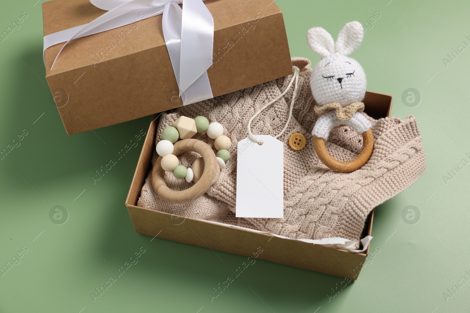 Photo of Different baby accessories, knitted sweater and blank card in box on green background