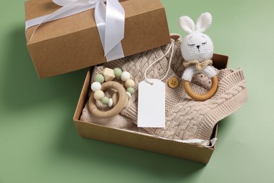 Photo of Different baby accessories, knitted sweater and blank card in box on green background