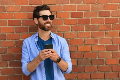 Happy man with smartphone near red brick wall. Space for text