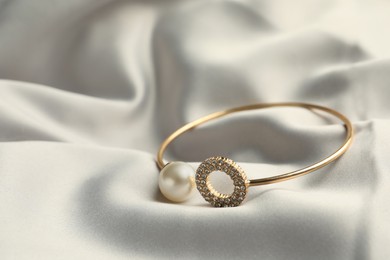 Photo of Elegant bracelet with pearl on grey silk, closeup