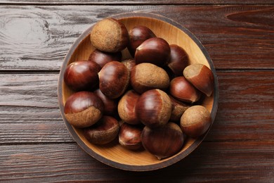 Photo of Sweet fresh edible chestnuts in bowl on wooden table, top view