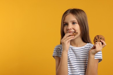 Photo of Cute girl eating chocolate chip cookies on orange background. Space for text