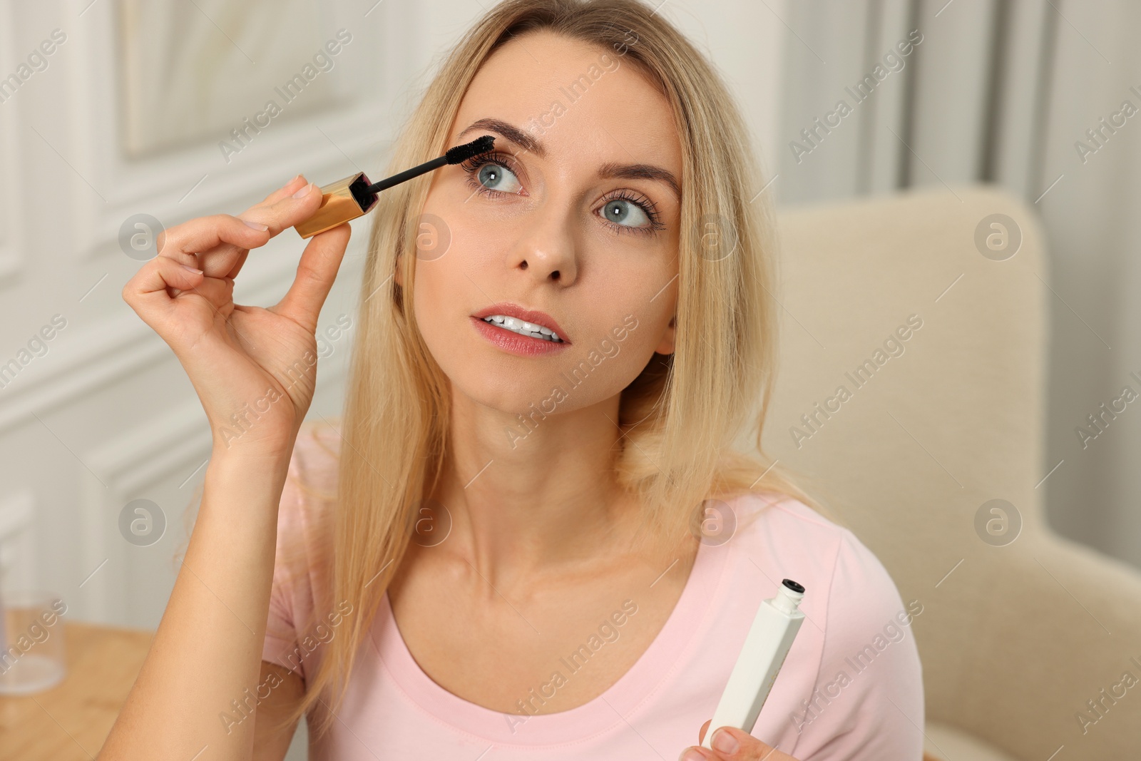 Photo of Beautiful woman applying mascara with brush indoors