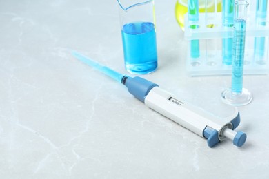 Photo of Laboratory analysis. Micropipette and different glassware with liquids on light grey marble table, space for text