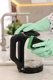 Photo of Woman cleaning electric kettle with sponge at countertop in kitchen, closeup