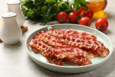 Photo of Plate with fried bacon slices, tomatoes, spices and parsley on grey textured table, closeup