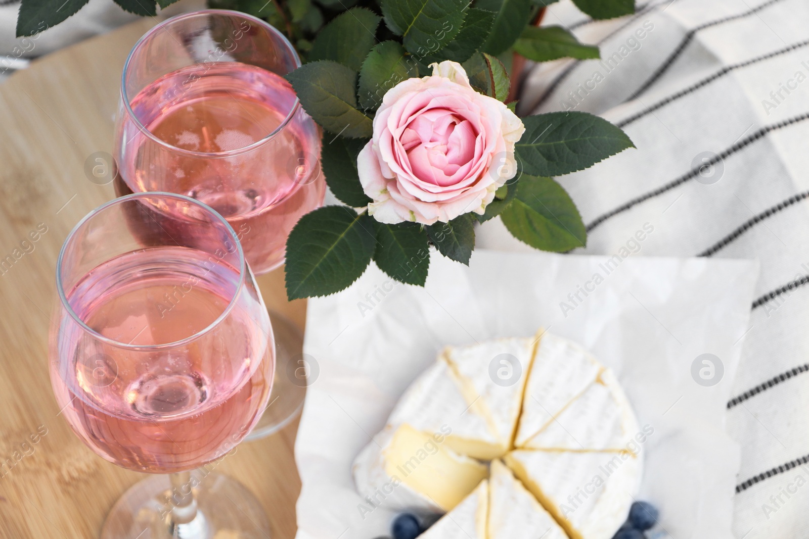 Photo of Glasses of delicious rose wine, flower and food on white picnic blanket