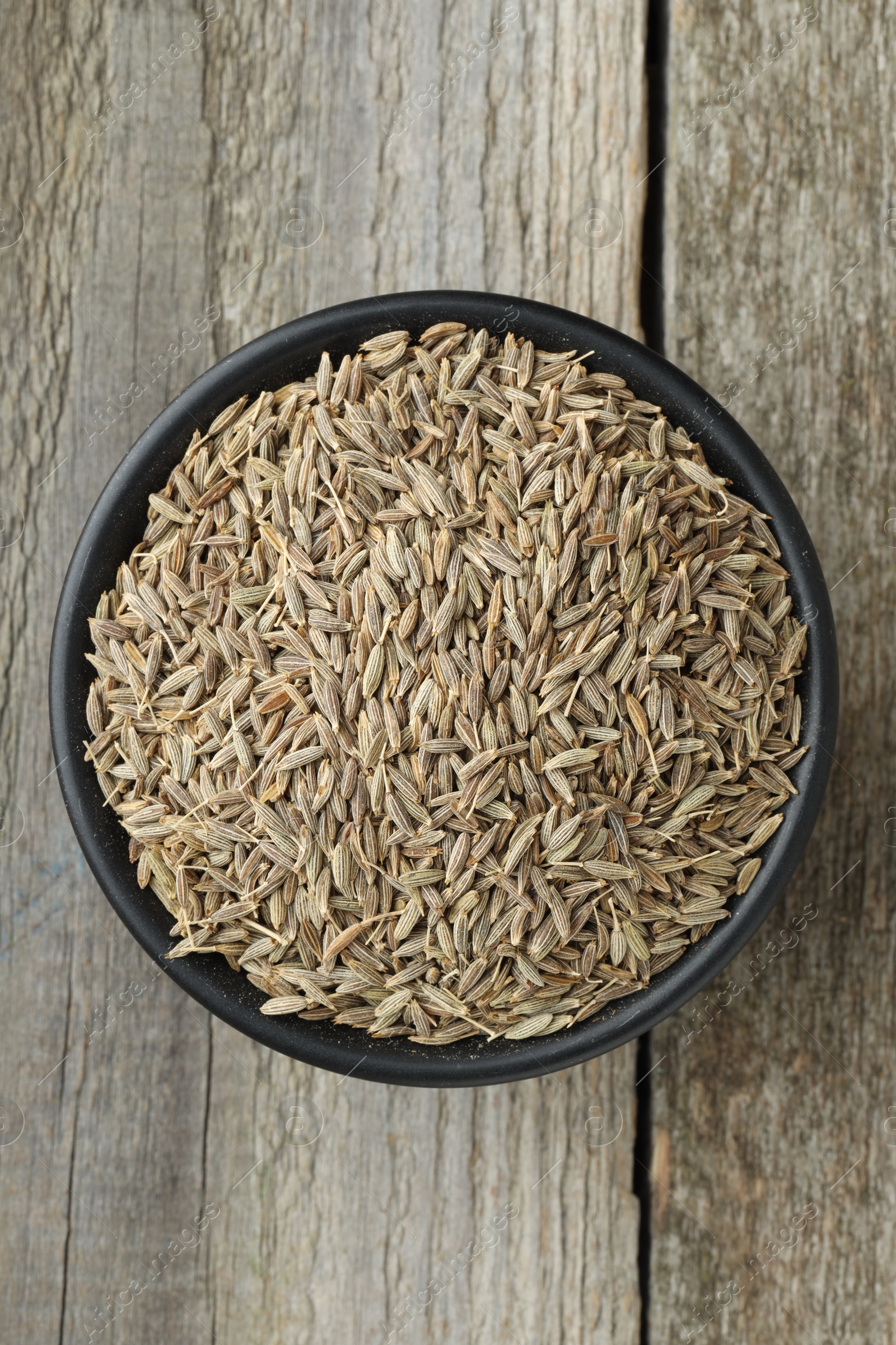 Photo of Bowl of caraway seeds on wooden table, top view