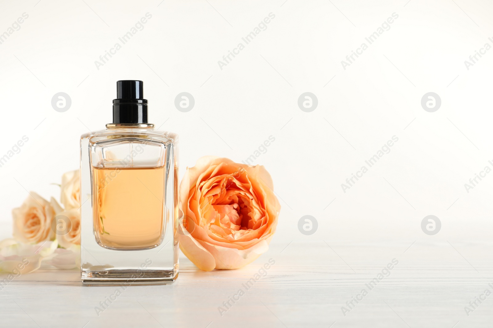 Photo of Elegant bottle of perfume and flowers on light background, space for text