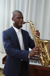 Photo of African-American man playing saxophone indoors. Talented musician