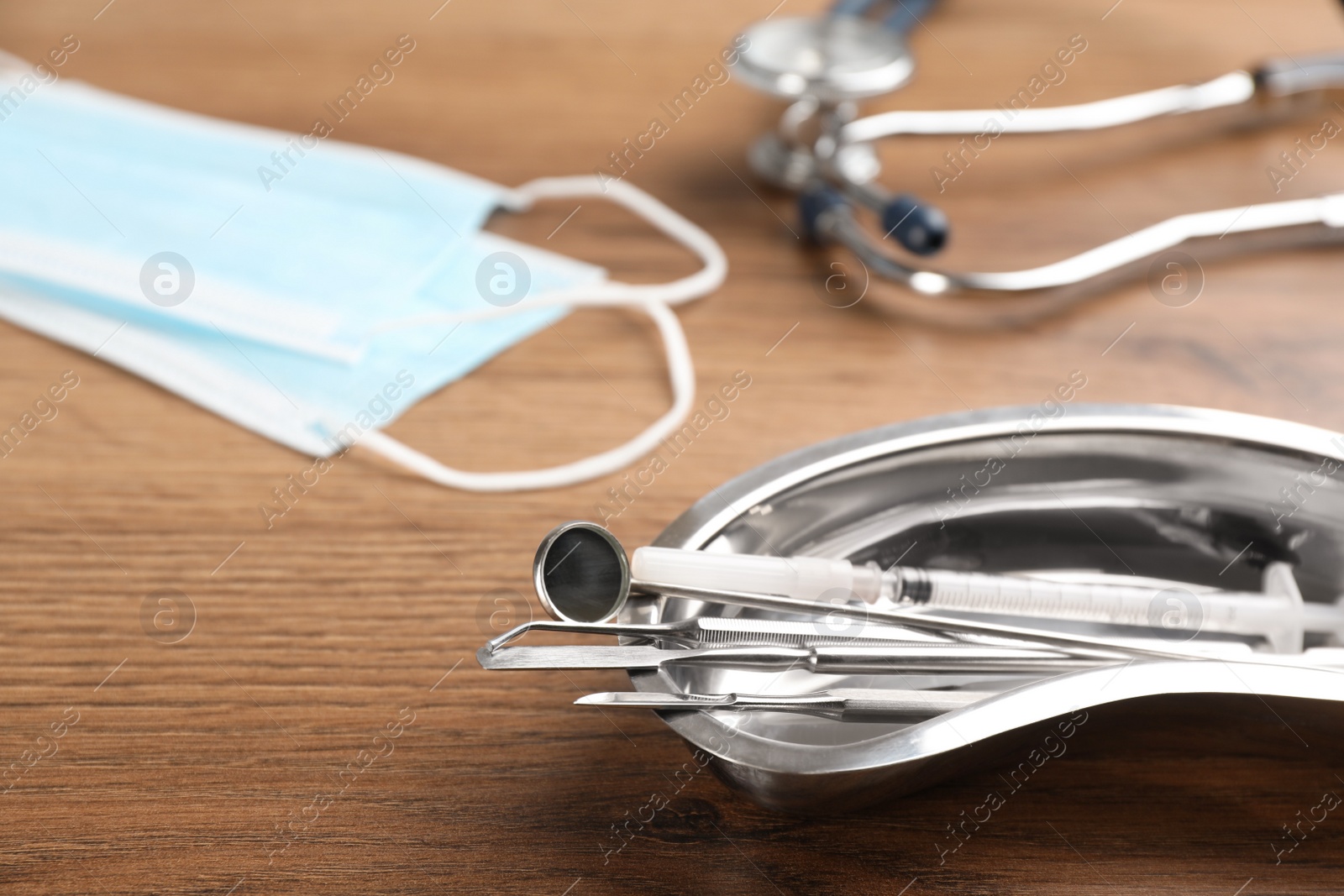 Photo of Kidney shaped tray with set of dentist's tools on wooden table, closeup. Space for text