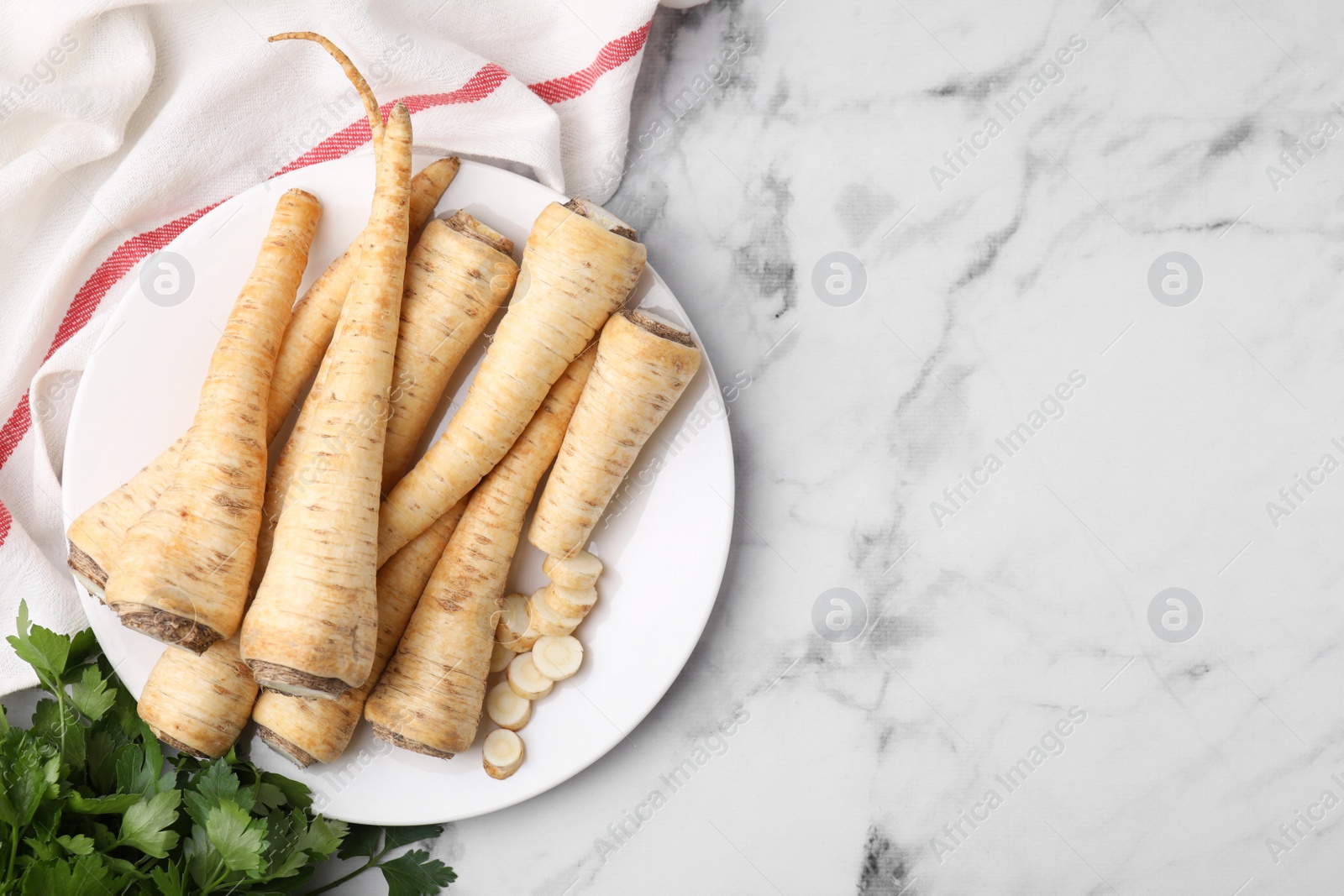 Photo of Raw parsley roots and fresh herb on white marble table, flat lay. Space for text