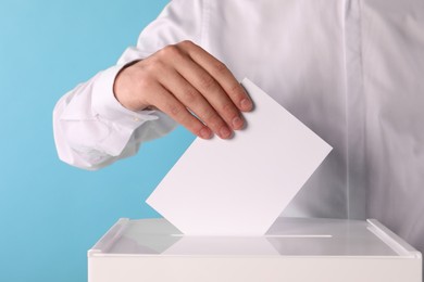 Photo of Man putting his vote into ballot box on light blue background, closeup