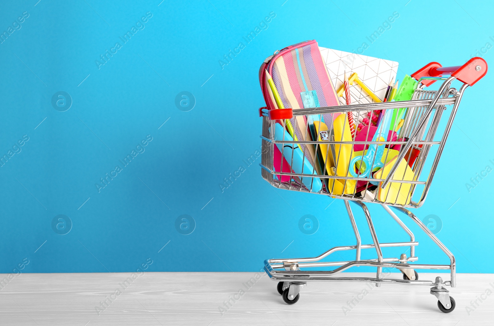 Photo of Small shopping cart with different school stationery on color background