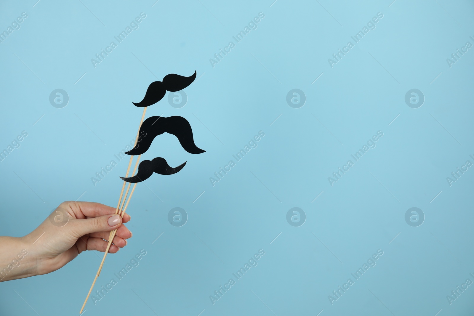 Photo of Woman with fake paper mustaches on light blue background, closeup. Space for text