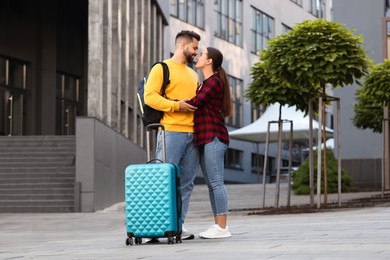 Photo of Long-distance relationship. Beautiful couple with luggage hugging outdoors
