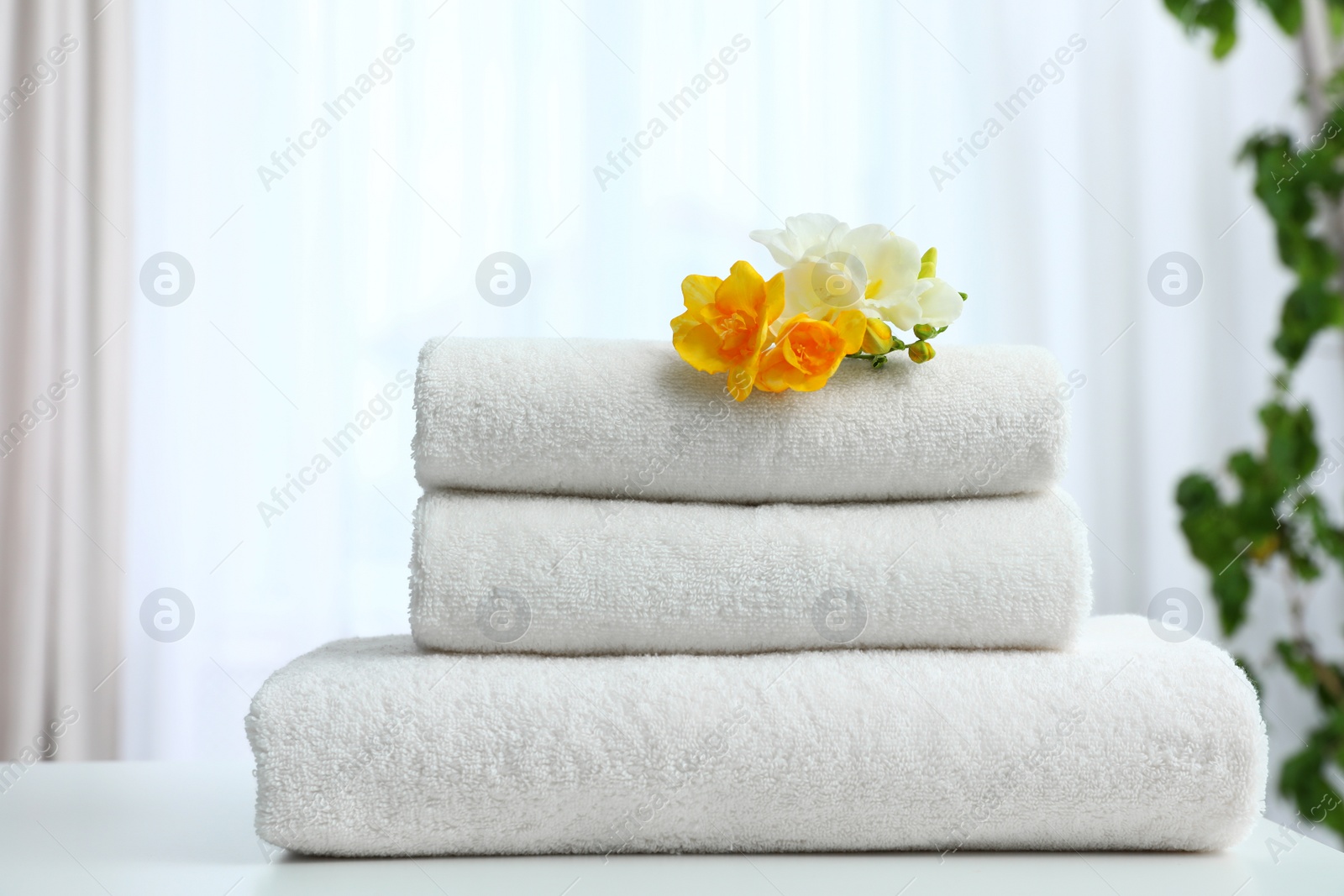 Photo of Stack of fresh towels with flowers on table indoors