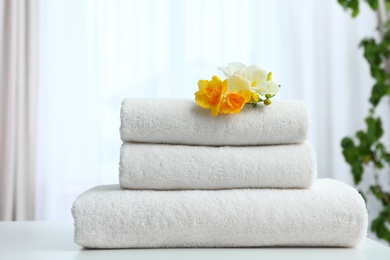 Stack of fresh towels with flowers on table indoors