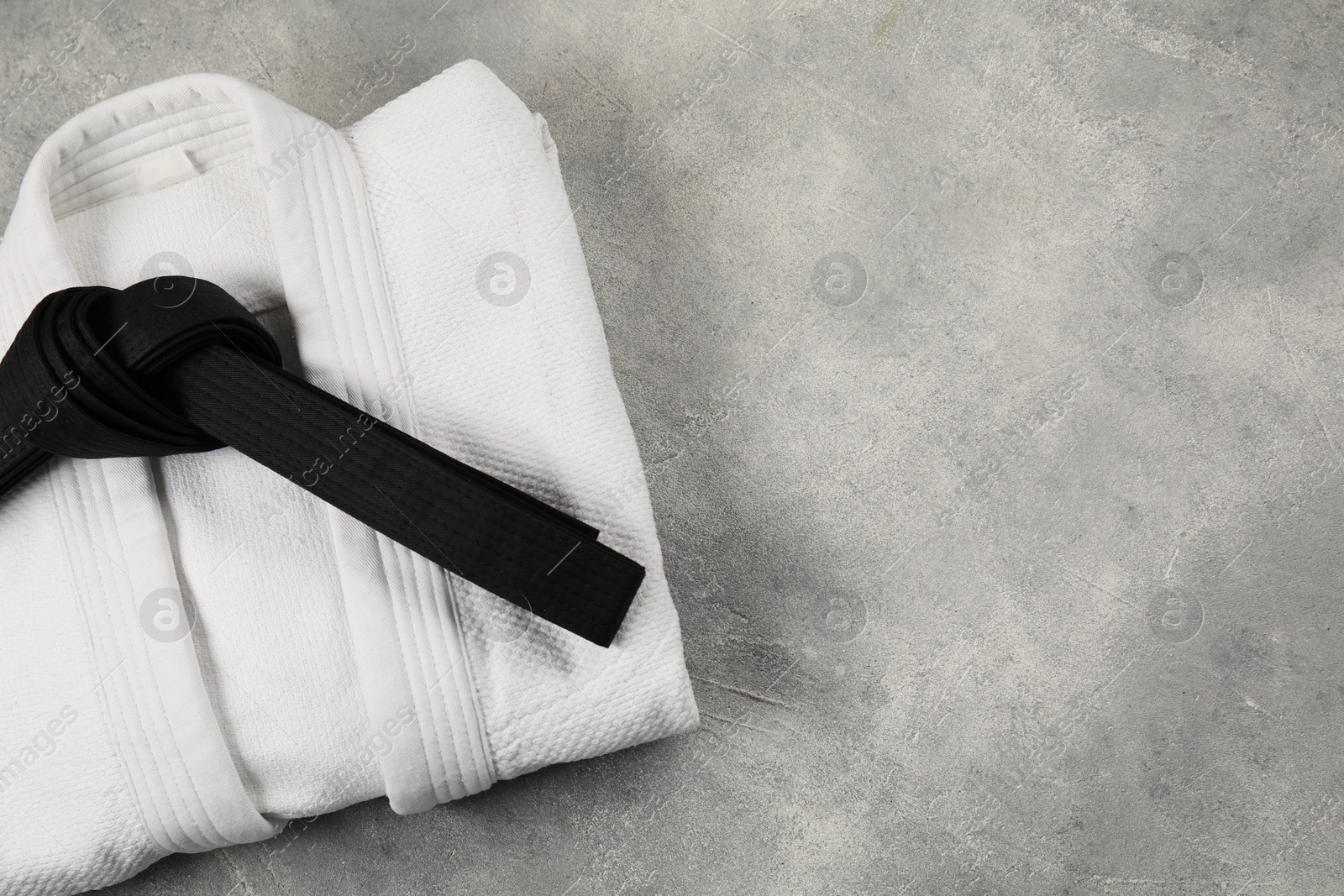 Photo of Black karate belt and white kimono on gray textured background, top view. Space for text