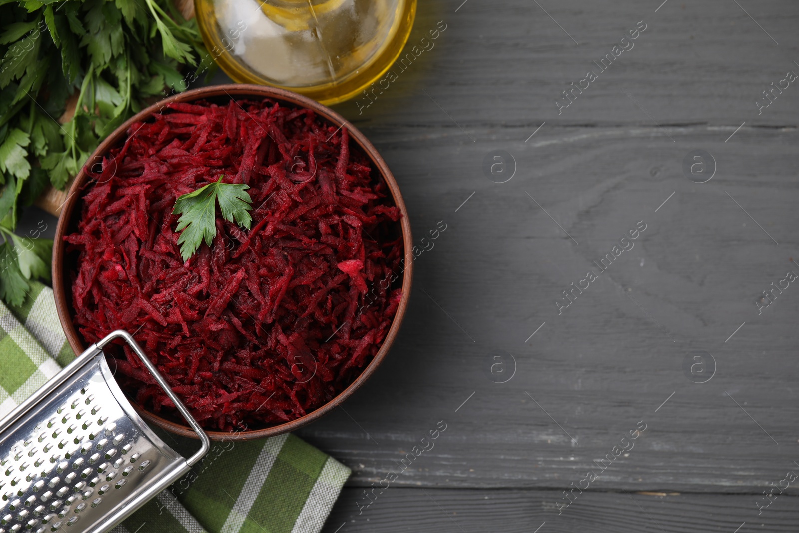 Photo of Grated red beet with parsley in bowl, grater and oil on gray wooden table, flat lay. Space for text
