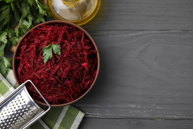 Photo of Grated red beet with parsley in bowl, grater and oil on gray wooden table, flat lay. Space for text