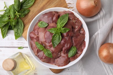 Photo of Bowl with raw chicken liver, basil and onions on white wooden table, flat lay