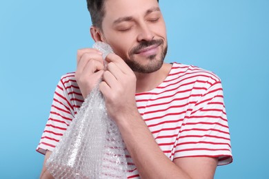 Man popping bubble wrap on light blue background, closeup. Stress relief