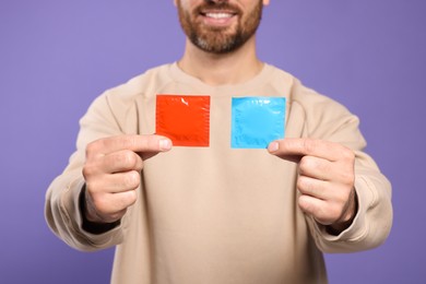 Photo of Man holding condoms on purple background, closeup. Safe sex