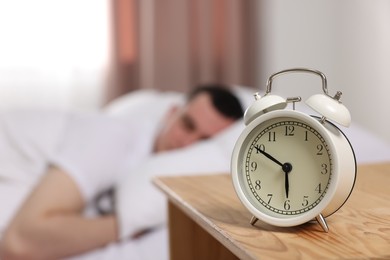 Man sleeping in bedroom, focus on alarm clock. Space for text