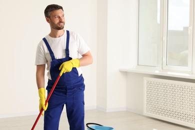 Photo of Man in uniform cleaning floor with mop indoors. Space for text