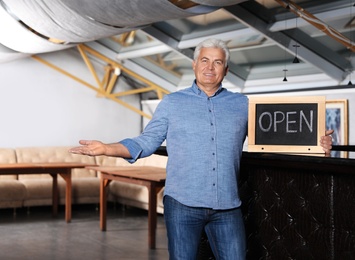 Photo of Senior business owner holding OPEN sign in his restaurant