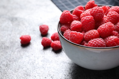 Photo of Delicious fresh ripe raspberries in bowl on grey table, closeup. Space for text