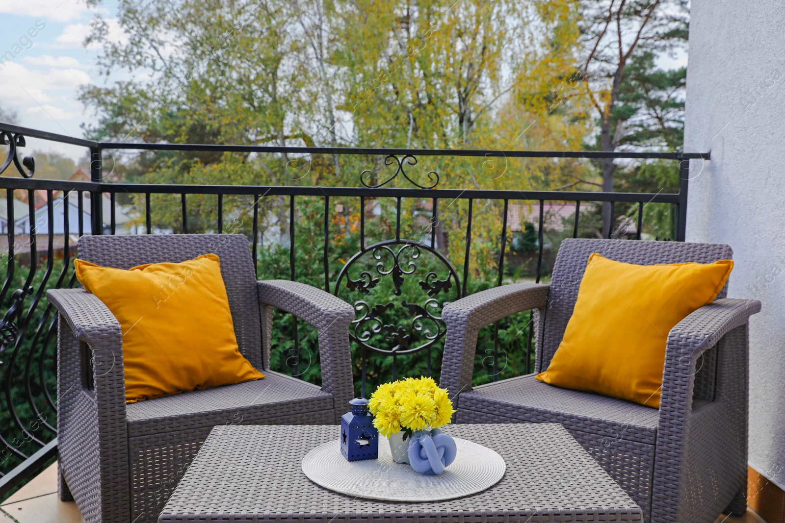 Photo of Orange pillows and yellow chrysanthemum flowers on rattan garden furniture outdoors