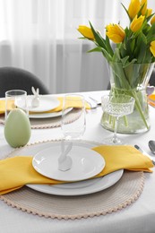 Photo of Festive table setting with glasses, burning candle and vase of tulips. Easter celebration