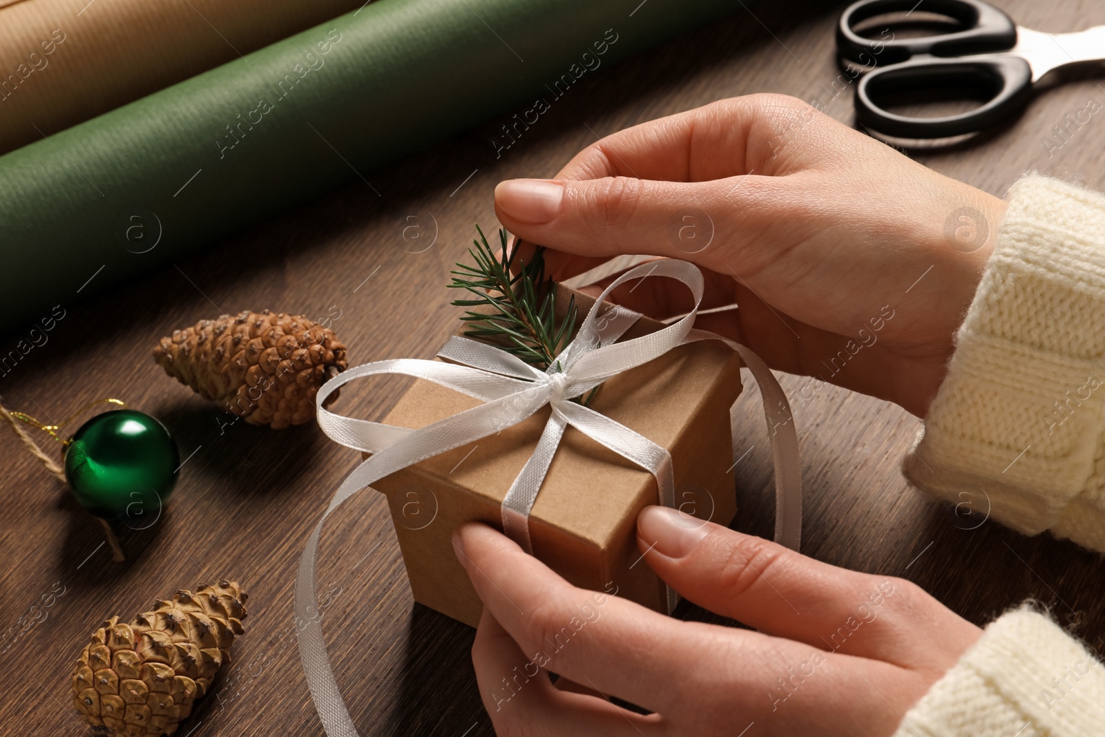 Photo of Woman decorating gift box at wooden table, closeup. Christmas present