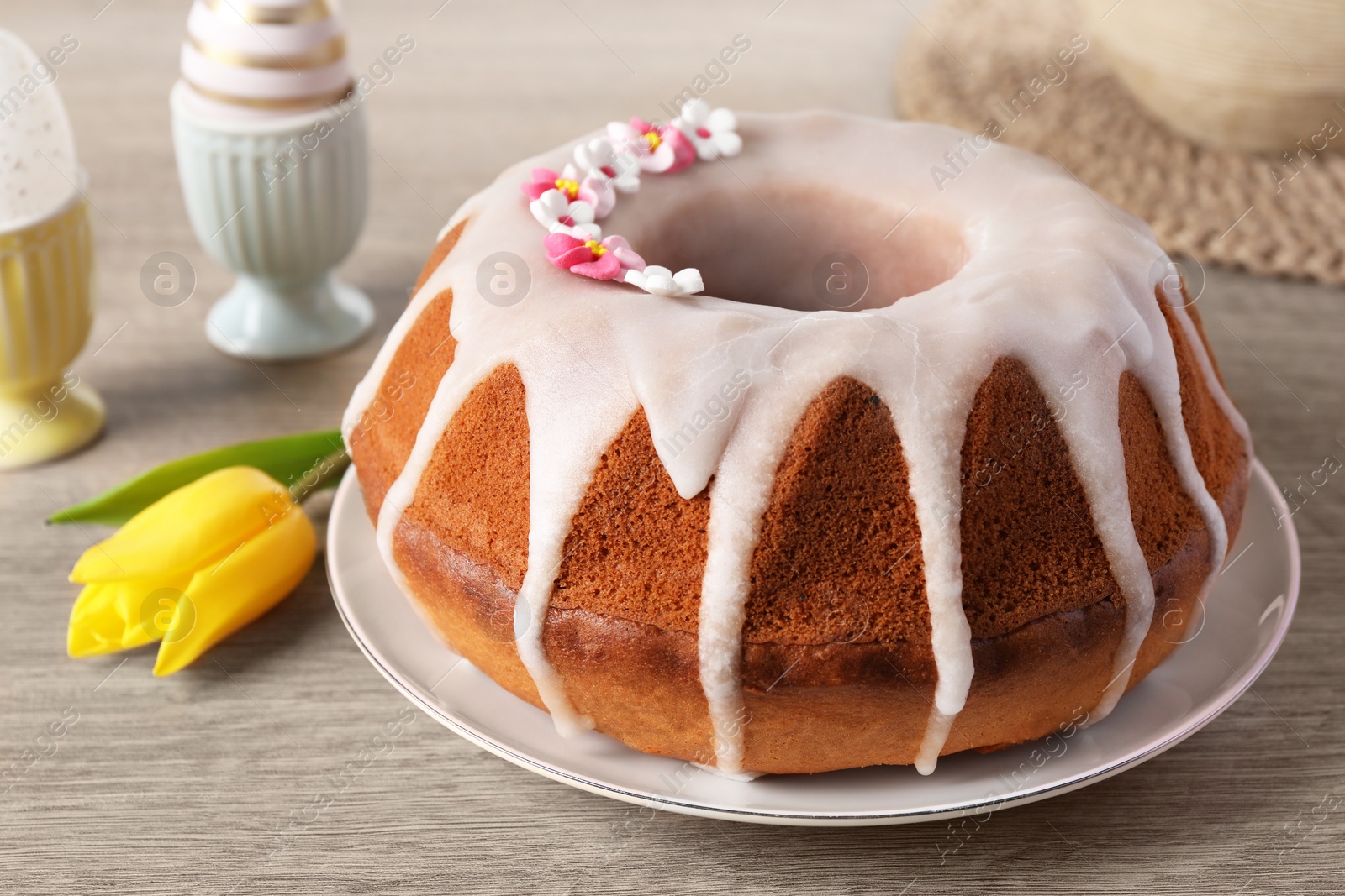 Photo of Delicious Easter cake decorated with sprinkles near beautiful tulip and painted eggs on wooden table, closeup