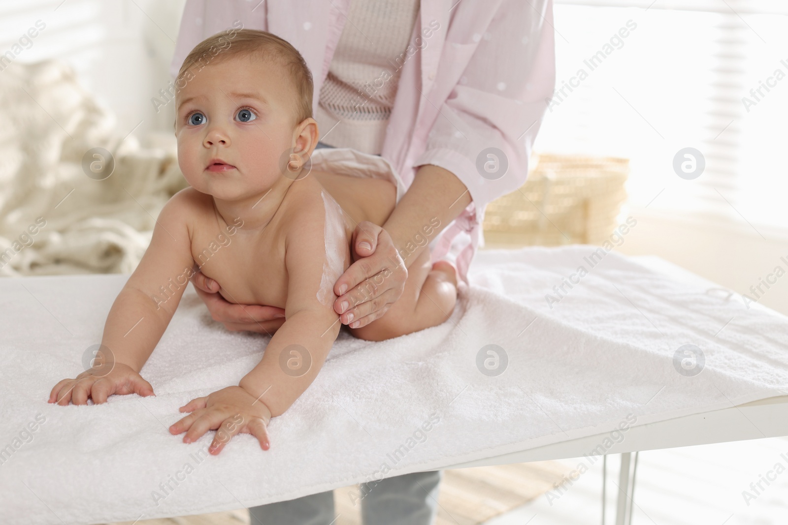 Photo of Mother applying body cream on her little baby at home, closeup