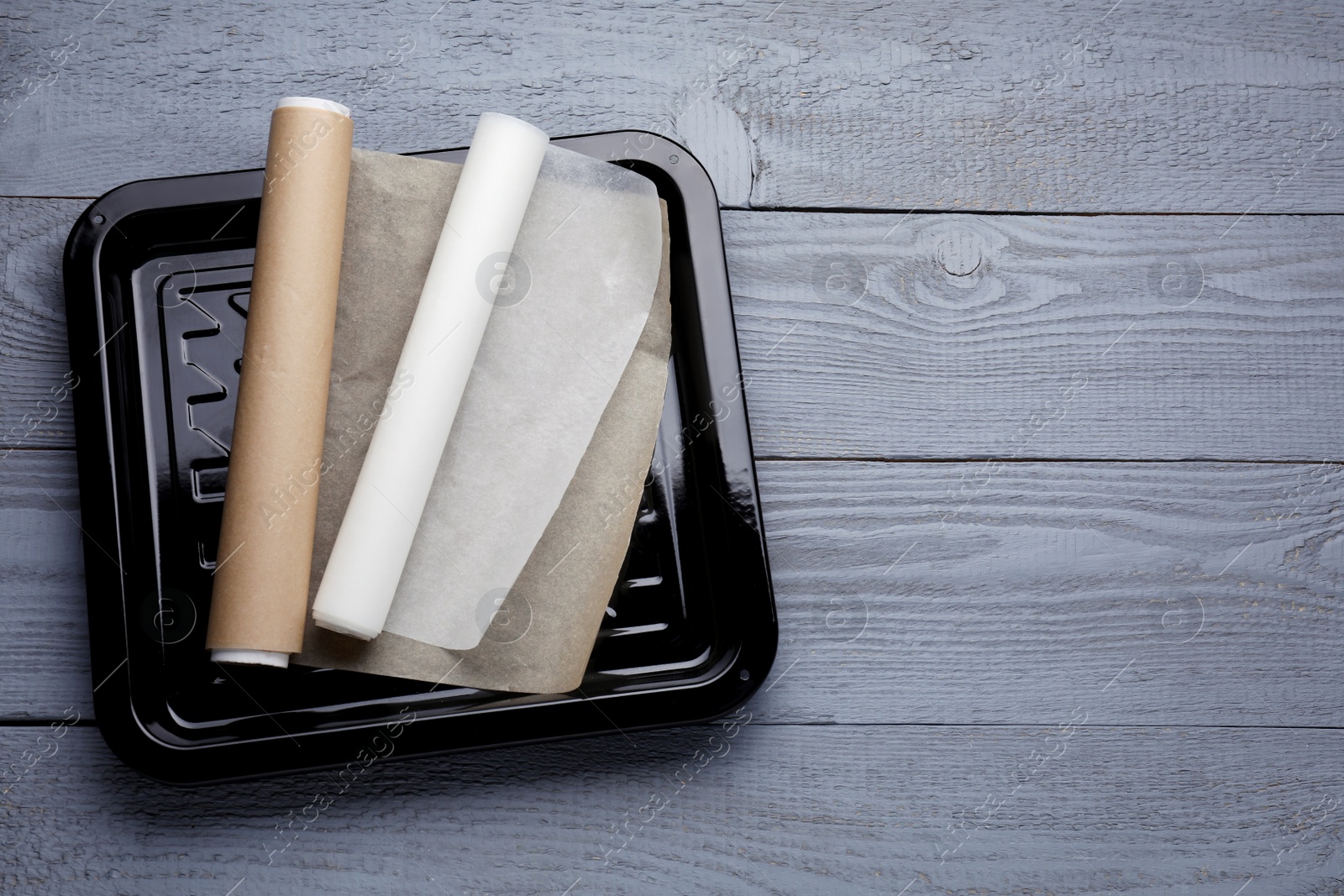 Photo of Rolls of parchment paper and baking pan on grey wooden table, top view. Space for text