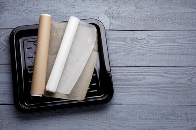 Rolls of parchment paper and baking pan on grey wooden table, top view. Space for text