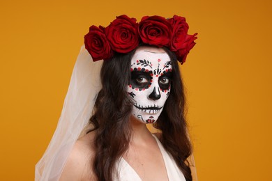 Photo of Young woman in scary bride costume with sugar skull makeup and flower crown on orange background. Halloween celebration