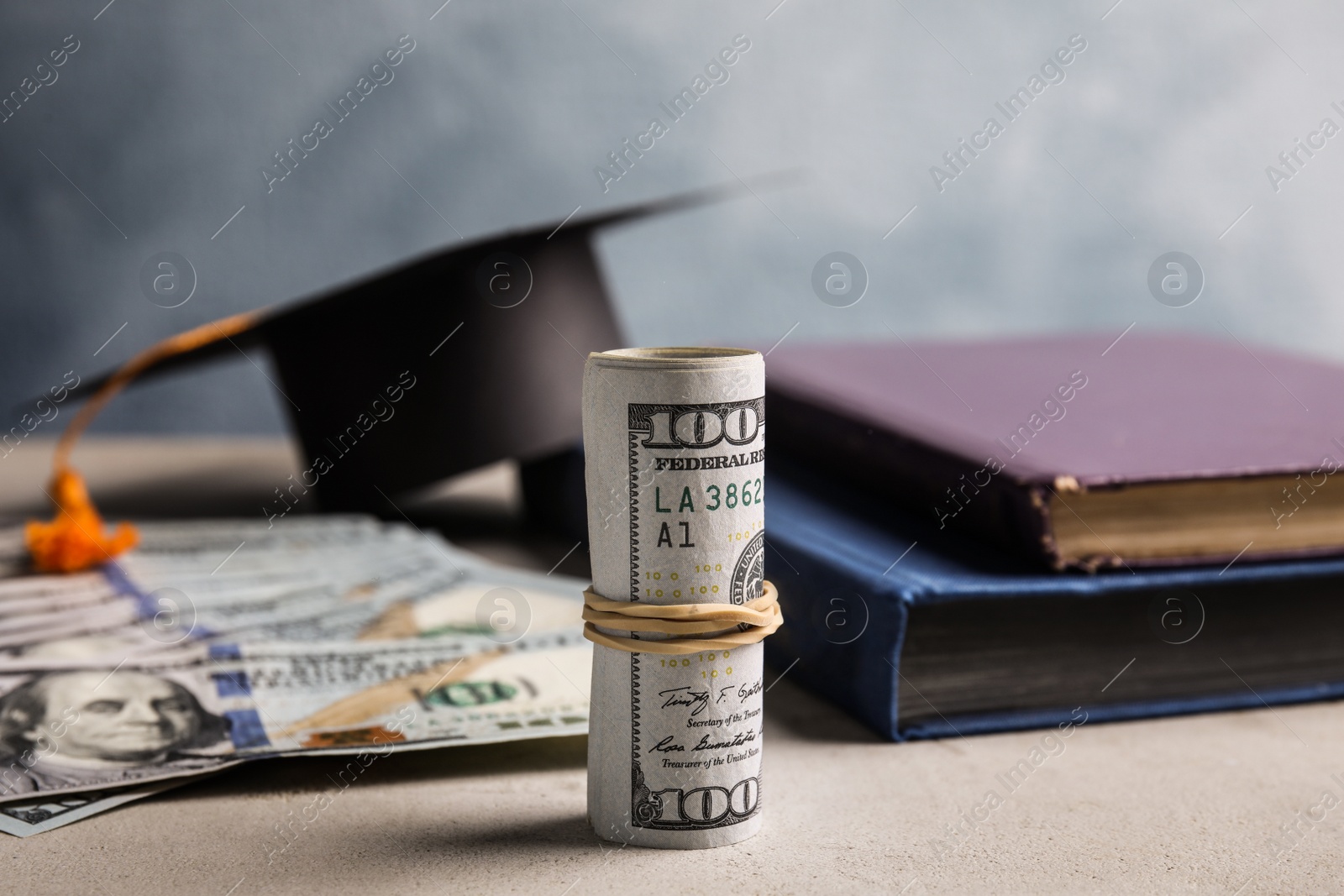 Photo of Dollar banknotes and student graduation hat on grey table. Tuition fees concept