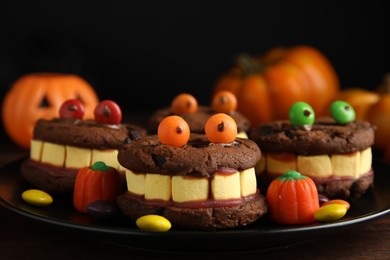 Photo of Delicious desserts decorated as monsters on wooden table, closeup. Halloween treat