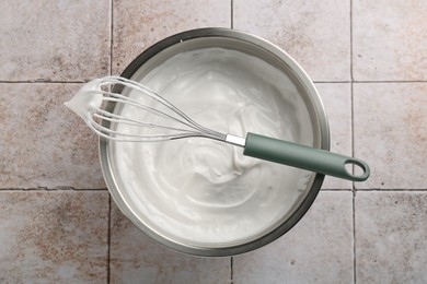 Photo of Bowl and whisk with whipped cream on tiled table, top view