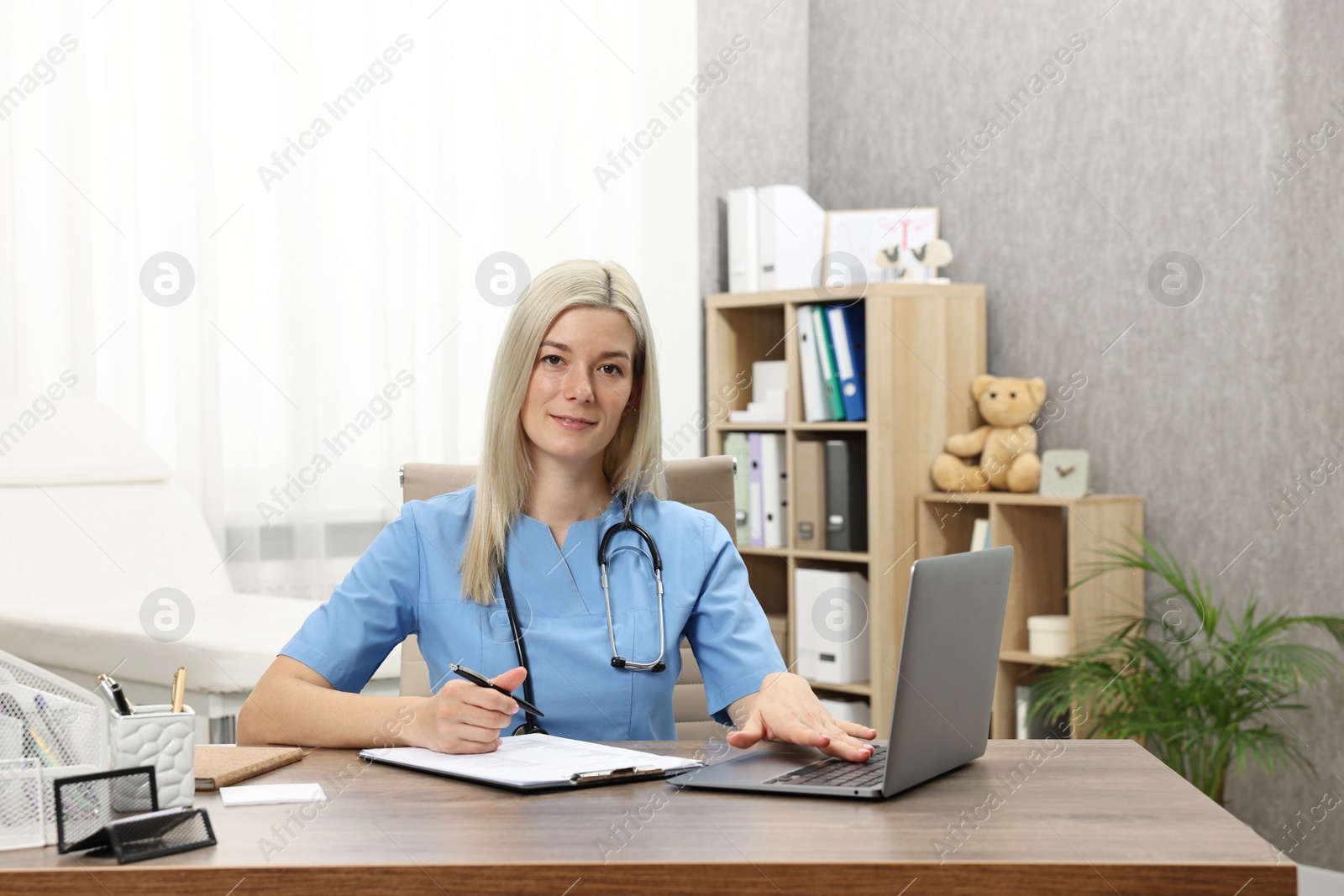 Photo of Doctor working with clipboard and laptop at table in clinic