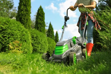 Photo of Woman cutting grass with lawn mower in garden on sunny day, closeup