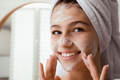 Photo of Beautiful teenage girl applying cleansing foam onto face in bathroom, closeup. Skin care cosmetic