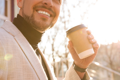 Photo of Businessman with cup of coffee on city street in morning, closeup