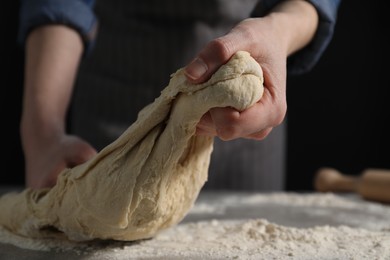 Photo of Making bread. Woman kneading dough at table on dark background, closeup. Space for text