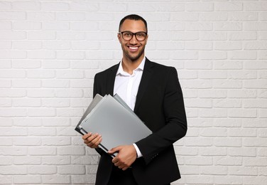 Photo of Young businessman in formal outfit with folders near white brick wall